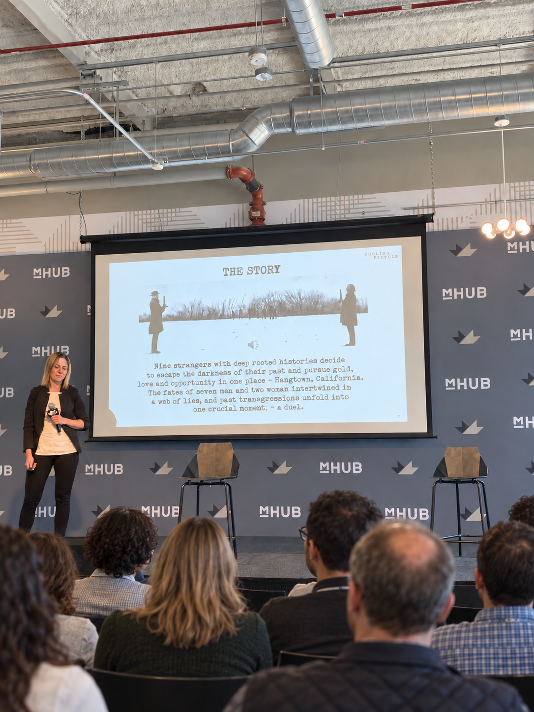 Anat Gotfried presenting on stage with an audience seated in front of her